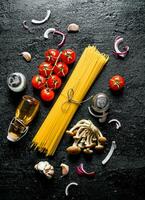 Raw spaghetti with onion slices, tomatoes, mushrooms and oil in a bottle. photo