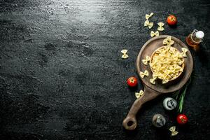 Raw Farfalle pasta in a bowl with the rosemary, tomatoes, spices and oil. photo