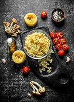 Raw farfalle and tagliatelle paste in a bowl on a cutting Board with mushrooms, tomatoes and spices. photo