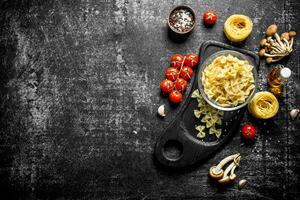Raw farfalle and tagliatelle paste in a bowl on a cutting Board with mushrooms, tomatoes and spices. photo