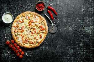 Sliced pizza with cherry tomatoes, onion rings and cheese sauce in bowl. photo