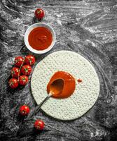 Preparation pizza. Rolled out dough with tomato paste and fresh tomatoes. photo