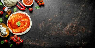 Preparation pizza. Rolled out dough with tomato paste, chili pepper and mozzarella. photo