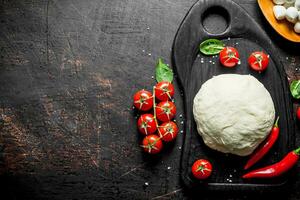 Pizza dough on a cutting Board with tomatoes, mozzarella and spinach. photo