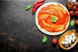 Preparation pizza. Rolled out dough with tomato paste, chili pepper and mozzarella. photo