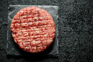 One Raw burger on a stone stand. photo