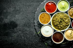An assortment of different sauces in bowls on a stone Board. photo