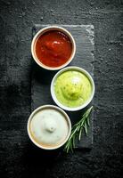 Guacomole sauce, tomato sauce and mayonnaise on a stone Board with rosemary. photo