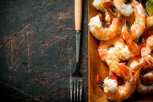 Fragrant shrimps on a wooden plate with a fork. photo