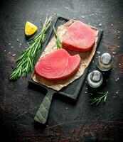 Pieces of raw tuna fillet on a cutting Board with rosemary, spices and lemon. photo