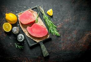 Pieces of raw tuna fillet on a cutting Board with rosemary, spices and lemon. photo