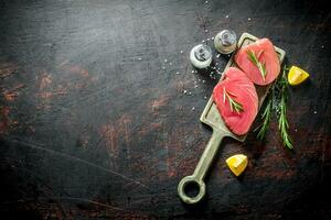 Pieces of fresh raw tuna on a cutting Board with spices, lemon and rosemary. photo