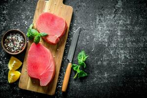 Fresco crudo atún filete en un de madera corte tablero con limón rebanadas, especias y menta. foto