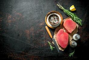 Pieces of fresh raw tuna on paper with spices, rosemary and a slice of lemon. photo