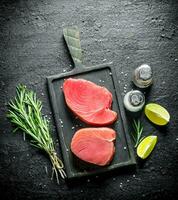 Fresh raw tuna steak on a cutting Board with rosemary, spices and lime slices. photo