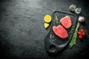 Fresh uncooked tuna steak on a cutting Board with tomatoes, rosemary, garlic, spices and lemon. photo