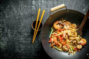 Freshly cooked Asian Udon noodles in a wok pan with soy sauce and chopsticks. photo