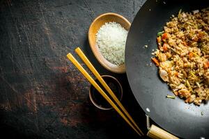 Chinese wok. Cooked rice in a wok pan and uncooked rice on a plate. photo