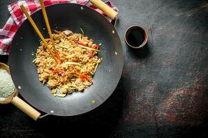 Freshly cooked rice with vegetables in a wok pan with raw rice on a plate and soy sauce. photo