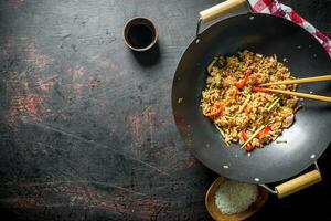 Freshly cooked rice with vegetables in a wok pan with raw rice on a plate and soy sauce. photo