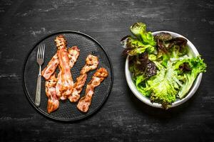 Fried bacon with greens. On black wooden background. photo