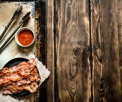 Fried bacon in a frying pan and tomato sauce. photo