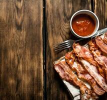 Fried bacon with tomato sauce. On wooden background. photo