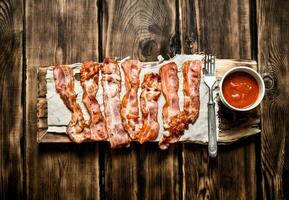 Fried bacon with tomato sauce. On wooden background. photo