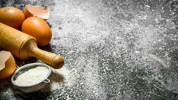 Baking background. Rolling pin with fresh eggs and flour on a rustic background. photo