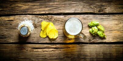 cerveza conjunto - cerveza en vaso, papas fritas, lúpulo y sal en de madera antecedentes. foto