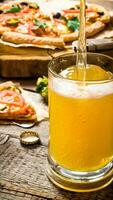 The breath of fresh beer being poured into glass. On the background of the pizza. photo