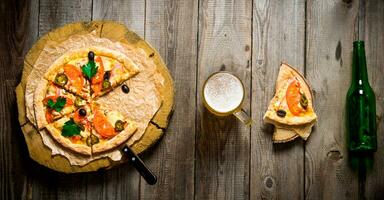 Pizza on wooden circle, beer, and a bottle on a wooden table. photo