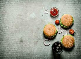 Three burgers with a soda on stone table. photo