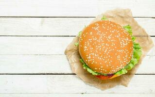 hamburguesa con carne de res, queso y vegetales en papel. foto