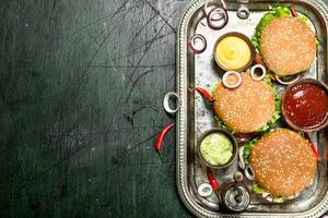 Burgers from fresh beef and vegetables with different sauces on a steel tray. photo