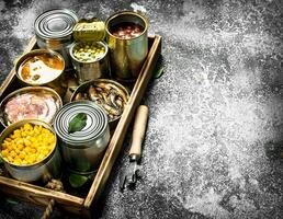 Various canned products in tin cans on a wooden tray. photo