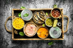 Various canned products in tin cans on a wooden tray. photo