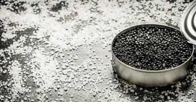 Black caviar in a jar with salt . On black wooden table. photo