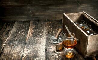 Cognac background. A bottle of cognac in a box with a glass and a cigar. photo