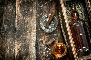 Cognac background. A bottle of cognac in a box with a glass and a cigar. photo