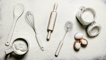 Baking background. Flour, eggs, and different tools - Beaters, spatula, rolling pin and a sieve. photo