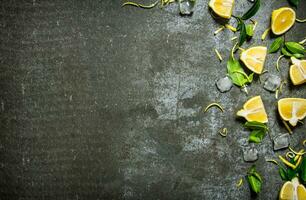 Slices of lemon, ice, leaves on stone table. photo