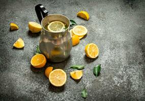 Cold lemonade in a jug with slices of lemon and green leaves. photo