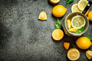 Cold lemonade in a jug with slices of lemon and green leaves. photo