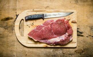 A piece of raw meat with knife on wooden Board. photo