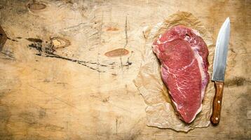 A large piece of raw meat with a butcher knife on the paper. photo