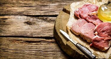 Fresh raw meat with knife and oil on a wooden stand. photo