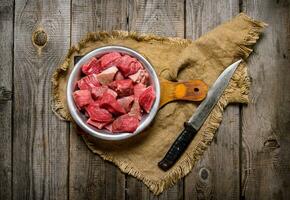 Cutting raw meat a large knife. On wooden table. photo