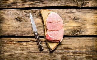 Raw steak with a knife on a wooden stand. photo