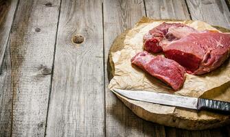 Cutting raw meat a large knife. On wooden table. photo